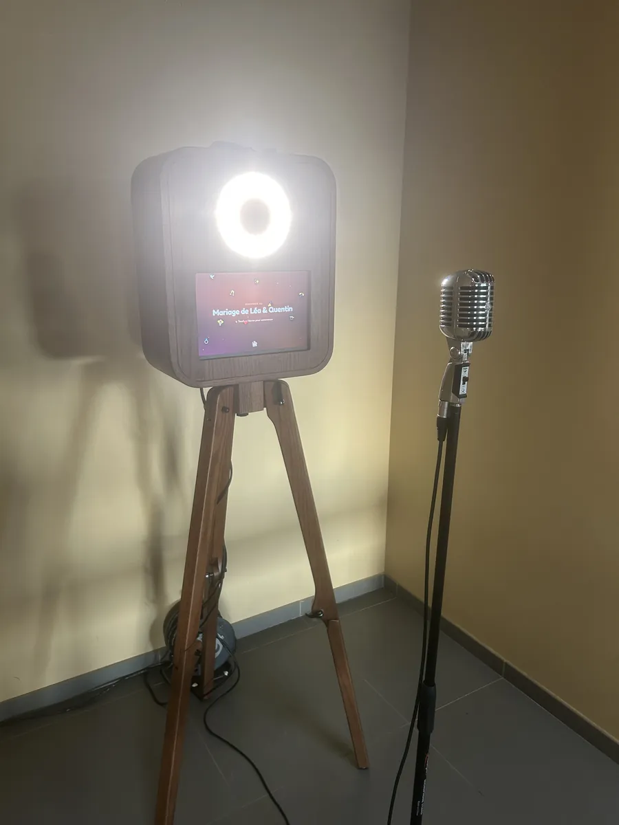 Borne photobooth vidéo sur trépied en bois, anneau lumineux allumé, écran d'accueil « Mariage de Léa & Quentin » et micro vintage sur pied, installée dans une salle de mariage à Sécheval (Ardennes)